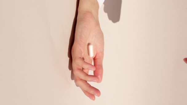 白薬の垂直的ショットはベージュの背景によって認識されていない人の手に落ちる ホメオパシー薬のサプリメント 高画質映像 — ストック動画