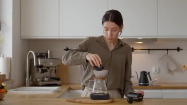 Genç bir kadın beyaz bir mutfakta kahve servisi, taze öğütülmüş kahve çekirdekleri kullanarak zengin ve aromatik bir kahve hazırlıyor..