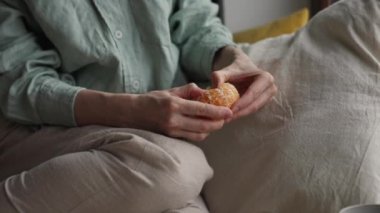 Kapalı çekim genç kadın elleri portakal rengi mandalinayı soyarken hüzünlü sisli bir günde pencerenin yanında otururken. Yüksek kalite 4k görüntü