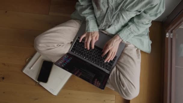 顶部角度拍摄的女性交叉腿坐在靠近窗户的地板上 在笔记本电脑上打字 并用电话在便条上打分 高质量的4K镜头 — 图库视频影像