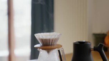 Sunucu bardağında modaya uygun kağıt filtresiyle taze demlenmiş v60 kahve hazırlıyorum. Beyaz oda arka planı. Buhar, filtredeki sıcak kahveden geliyor. Yüksek kalite 4k görüntü
