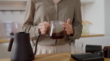 Genç bir kadın sunucuda el yapımı V60 kahve yapıyor. Beyaz, rahat bir evin içinde, mutfakta. Yüksek kalite 4k görüntü