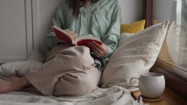 Kitap sayfalarını çeviren kadın eli, yağmurlu bir günde evde yastığın yanında oturan kız. Yüksek kalite 4k görüntü