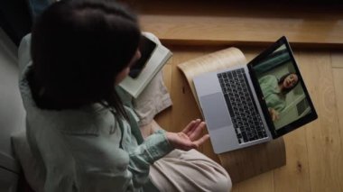 Üst düzey çekici, gülümseyen kadın kendini çevrimiçi kursa kaydediyor ve evde, oturma odasındaki ahşap zeminde oturuyor. Yüksek kalite 4k görüntü