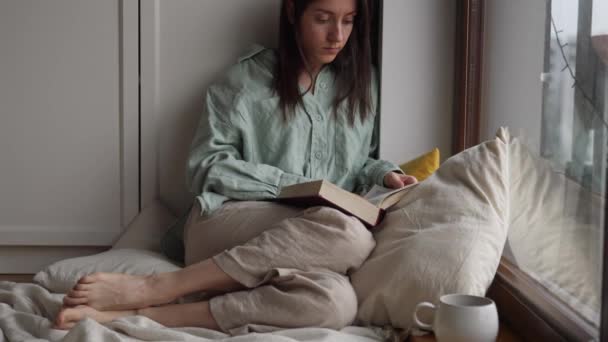 Atraente Jovem Leitura Livro Feminino Virando Páginas Sentadas Perto Janela — Vídeo de Stock