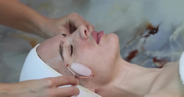 サロンのスキンケアコンセプトの顔の皮別のアンチエイジングのために彼女の頬にクォーツローラーマッサージを使用して女性のクローズアップ肖像 高品質4K映像 — ストック動画