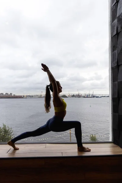 Kahraman pozunda yoga yapan genç bir kadının silueti. Karantina ev antrenmanı kavramı. Reklam alanı. Yüksek kalite fotoğraf