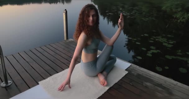 ヨガをしているビューティフーの女の子 湖のそばのジェティー 朝のヨガ ピラティスだ 落ち着いて アサナ 高品質4K映像 — ストック動画