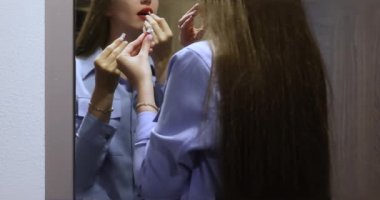 Uzun saçlı güzel bir kadın dudaklarını kırmızı rujla boyar, aynanın yansımasına bakar, randevuya ya da partiye hazırlanır. Aynanın önünde kadın esmer ve makyaj portresi. Yüksek kalite 4k