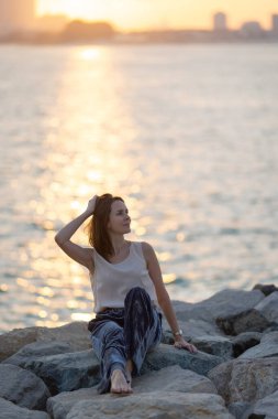 Güneş doğarken yoga meditasyonu yapan bir kadın. Sahilde ya da deniz kenti arka planında sabah yogası. Yüksek kalite fotoğraf