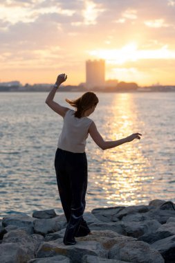 Güneş doğarken yoga meditasyonu yapan bir kadın. Sahilde ya da deniz kenti arka planında sabah yogası. Yüksek kalite fotoğraf
