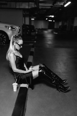 amazing girl eats fast food, drink sodas, eat burger Fashionable beautiful woman wears trendy sunglasses in a fashion black dress with leather black shoes and a stylish bag sits on a walkway in an un