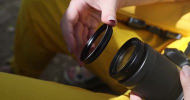 Womans hand brings the photo filter to the camera lens and attaches it. Female hand sets a photo filter to the camera lens. Polarizing filter for camera lens in photography large diameter photo filter
