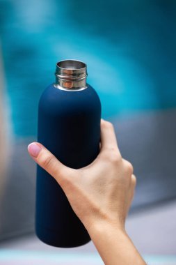 Close-up of female hand holding reusable steel thermo water bottle isolated on background of cyan color with copy space. High quality photo