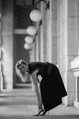 Lüks siyah elbiseli güzel, beyaz, sarışın bir kız modern bir şehirdeki bir parkın arka planında duruyor. Geleceğin şehrinde yeşillik ve beton. Yüksek kalite fotoğraf