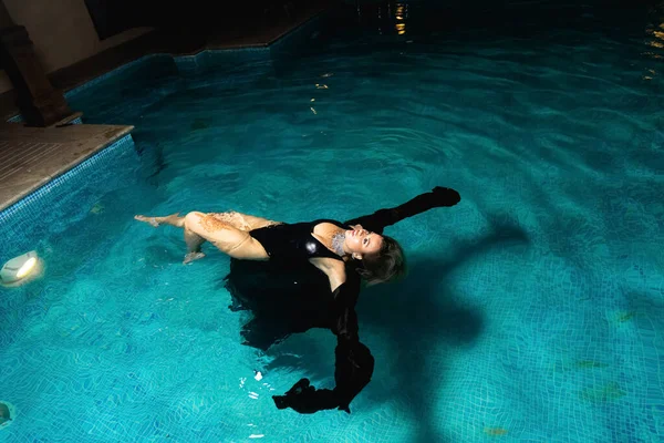 黒水着のセクシーな女の子がパーティーでプールのそばで夜ポーズ 水の中の魅力的なモデル 低光条件下でのフラッシュ撮影 高品質の写真 — ストック写真
