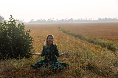 Tercümesi: Hint elbiseli güzel beyaz bir kız Asya 'da bir pirinç tarlasında meditasyon yapar ve güneşin doğuşunu selamlar. Doğayla bütünleşme. Güne doğru bir başlangıç. Yüksek kalite fotoğraf