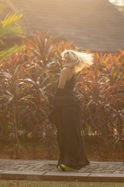 Güzel beyaz bir sarışın siyah bir şapka takarak doğada yürüyor. Pahalı bir otelin arazisinin lüksü. Yüksek kalite fotoğraf