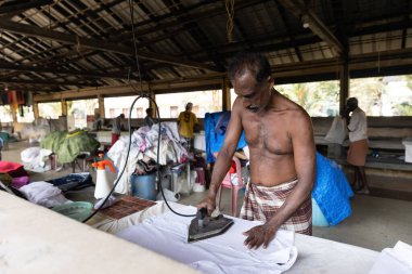 KOCHI, INDIA - 28 HAZİRAN 2023: Bir adam yerel çamaşırhanedeki çamaşırları elle ütülüyor. Yüksek kalite fotoğraf