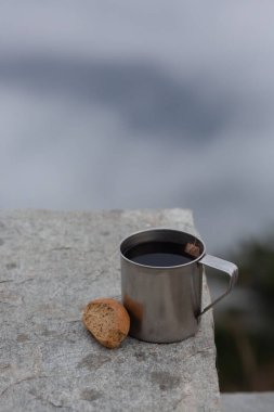 Çelik bir kamp bardağı ve bulutların üzerinde ekmek resmi. Engebeli çelik bardak açık hava maceraları için uygundur ve ekmek basit ama tatmin edici bir yemektir. Yüksek kalite fotoğraf