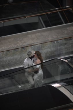 Uluslararası düğün. Açık renk saçlı, beyaz takım elbiseli yakışıklı, koyu tenli damat güzel, beyaz saçlı gelini kucaklıyor. Yüksek kalite fotoğraf
