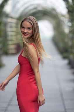 Kırmızı elbiseli, külotlu çoraplı ve topuklu ayakkabılı güzel sarışın kız şehir meydanında poz veriyor. Yüksek kalite fotoğraf