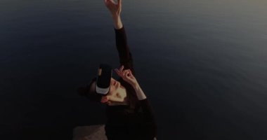 Genç kadın şafak ışıklarının sihirli atmosferinde sanal ya da artırılmış gerçeklik gözlüğü kullanıyor, dijital etkileşimli sanat performansında kadın kulaklık kullanıcısı, geleceğin eğlencesi. Yüksek kalite 4k görüntü