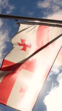 Güneş ışınları Georgia 'nın bayrağını dalgalandırıyor bulutlu mavi gökyüzünün arka planına doğru. Georgia 'nın bağımsızlık günü. Yüksek kalite 4k görüntü