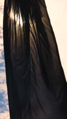 Amblemsiz siyah bir bayrak güneş yansımalarıyla mavi gökyüzüne doğru dalgalanıyor. Yüksek kalite 4k görüntü