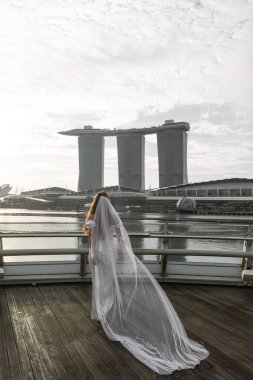Gelinler, Singapur şehrinin arka planına karşı bir perdeyle geri döndüler. Duvak rüzgarda dalgalanıyor. Yüksek kalite fotoğraf