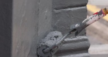 Bir müteahhit, büyük bir şehirde gün ışığında bir sokağa gri boyayla duvar boyuyor. Video yavaş çekimde. Tekerlek aleti yukarı aşağı hareket ediyor. Hareketler tekrarlanıyor. Yüksek kalite 4k görüntü