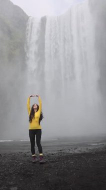 İzlanda 'da mutluluk ve neşe dolu bir şelalenin önünde dönen bir kız. Yüksek kalite 4k görüntü
