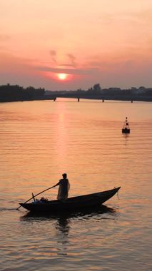 Asya 'daki bir nehirde şafak vakti balıkçı teknesinin arka planında bir balıkçının silüeti vardı. Yerel balıkçılık uygulamaları. Yüksek kalite 4k görüntü