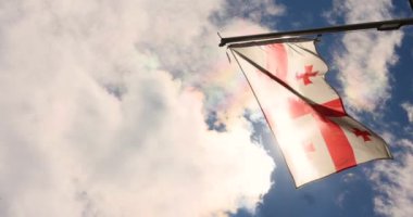 Güneş ışınları Georgia 'nın bayrağını dalgalandırıyor bulutlu mavi gökyüzünün arka planına doğru. Georgia 'nın bağımsızlık günü. Yüksek kalite 4k görüntü