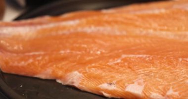 Büyük kırmızı balık fileto somon balığı. Tabakta tuzla buz edilmiş. Çiğ somon fileto dokusu kapanıyor. Sürgülenmiş taze kesilmiş, yağlanmış ve marine edilmiş somon balığı siyah tavada. Yüksek kalite 4k görüntü