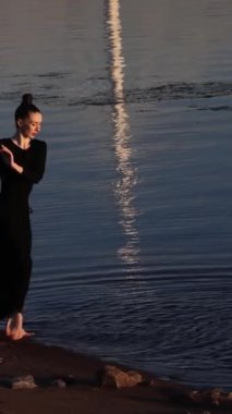 Balerin, şafakta okyanusun ya da gölün arka planında dans ediyor. Çağdaş dans sıçraması. Yüksek kaliteli FullHD görüntüler