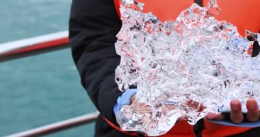 Kuzey Kutbu ya da Kuzey Bölgelerinde Turizm. Bir gezgin bir buz dağından bir parça buz tutuyor. İklim değişikliği fikri. Buzulların erimesi. Yüksek kalite 4k görüntü