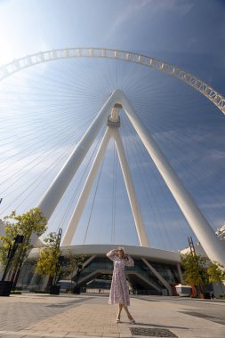 Beyaz şapkalı ve elbiseli güzel bir beyaz kız Dubai şehrinin arka planında duruyor. Parlak gündüz güneşi parlıyor. Mavi gökyüzü ile yaz konsepti. Yüksek kalite fotoğraf