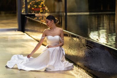 Güzel gelin elbisesinin kenarını düzeltir. Lüks elbiseli gelin. Düğünde zarif bir bayan. Arka Arka Arka Tarafı Çıplak Uzun Elbiseli. Fantezi Moda Gelini Işık Bakıyor. 