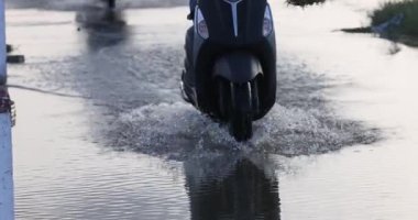 Scooter su basmış bir yolda ilerliyor. Mobiletler. Sel sonrası araçlar. Şiddetli yağmurdan sonra yol tamamen suyla kaplanır.
