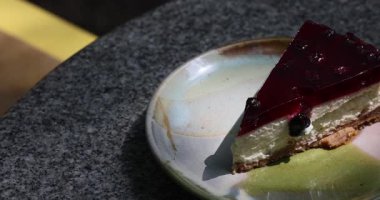 Masanın üzerinde güneş tarafından aydınlatılmış yabanmersinli bir cheesecake var. Bu lezzetli tatlı moralini düzeltecek ve süzme peynir içerecek. Yüksek kalite 4k görüntü
