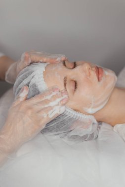 Bir kozmetik uzmanı güzel bir kadının yüzüne köpük sürer. Yüksek kalite fotoğraf