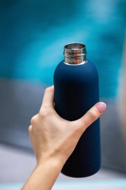 Yeniden kullanılabilir çelik termo su şişesini tutan kadın elinin yakın plan fotoğrafı. Arka planda, kopyalama alanı olan Cyan renklerinde izole edilmiş. Yüksek kalite fotoğraf
