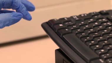 Sağlık çalışanları mavi bir eldiven verip tozlu siyah bir klavyeye yazı yazıyorlar. Yüksek kalite 4k görüntü