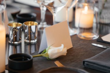 Lüks siyah bir masada sofistike bir kutlama için şık bir masa. Altın şamdanlar, şarap kadehleri, beyaz güller, peçeteler ve bir kağıt isim kartı... İnce bir atmosfer yaratır..