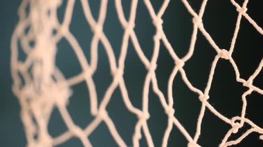 Kalın ipliklerden yapılmış beyaz bir ağa yakın plan, muhtemelen futbol ya da balık tutmak için kullanılıyor. Yumuşak ışıkta vurgulanan ağın detaylı dokusu ve yapısı. Yüksek kalite 4k görüntü