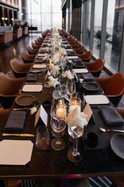 Beyaz güller, bardaklar, peçeteler ve siyah tabaklar olan zarif bir siyah masa manzarası. Perspektif uzaklığa doğru yol alır. 