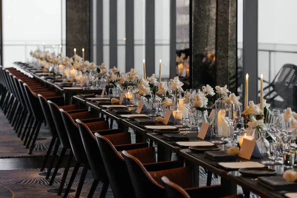  Beyaz güller, el yapımı tabaklar, doğal ahşap sandalyeler ve gözlüklerle işlenmiş siyah masa manzarası. Sofistike bir ortam için taze çiçeklerle süslenmiş zarif bir dekor. Yüksek kalite fotoğraf