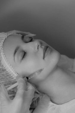 Açık tenli bir kadının estetik ameliyat sırasında botoks yaptırdığı siyah beyaz bir fotoğraf. Klinik ortamda estetik tıp ve güzellik tedavisi. Yüksek kalite fotoğraf