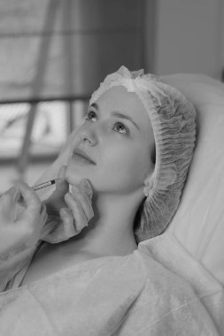 Açık tenli bir kadının estetik ameliyat sırasında botoks yaptırdığı siyah beyaz bir fotoğraf. Klinik ortamda estetik tıp ve güzellik tedavisi. Yüksek kalite fotoğraf
